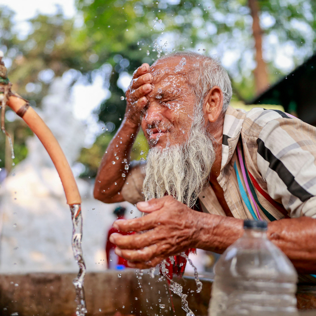 Old man splashes water from a fountain on his face.