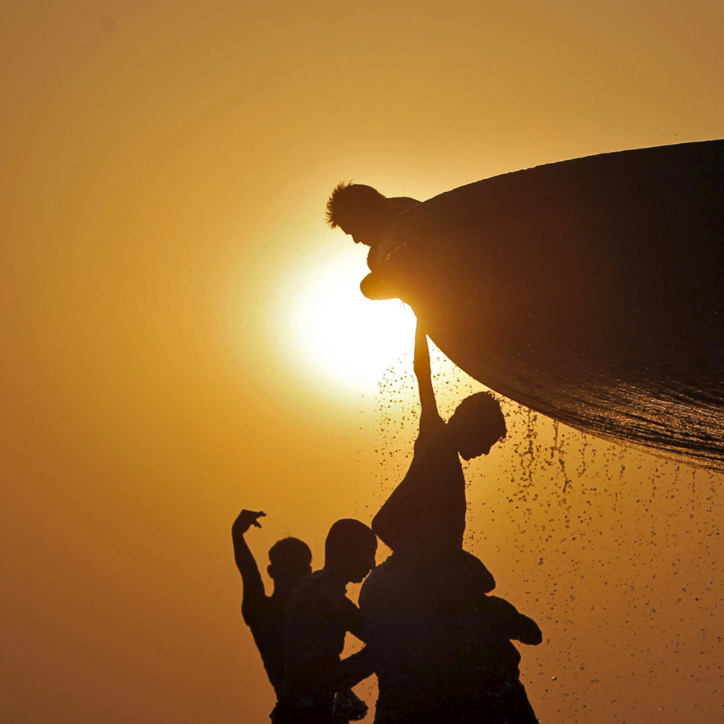 Silhouette of children playing in public fountain during sunset.