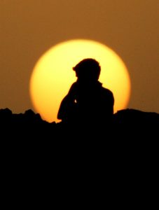 Image of a laborer resting, silhouetted against hot evening sun. Outdoor laborers face great economic impacts from heat.