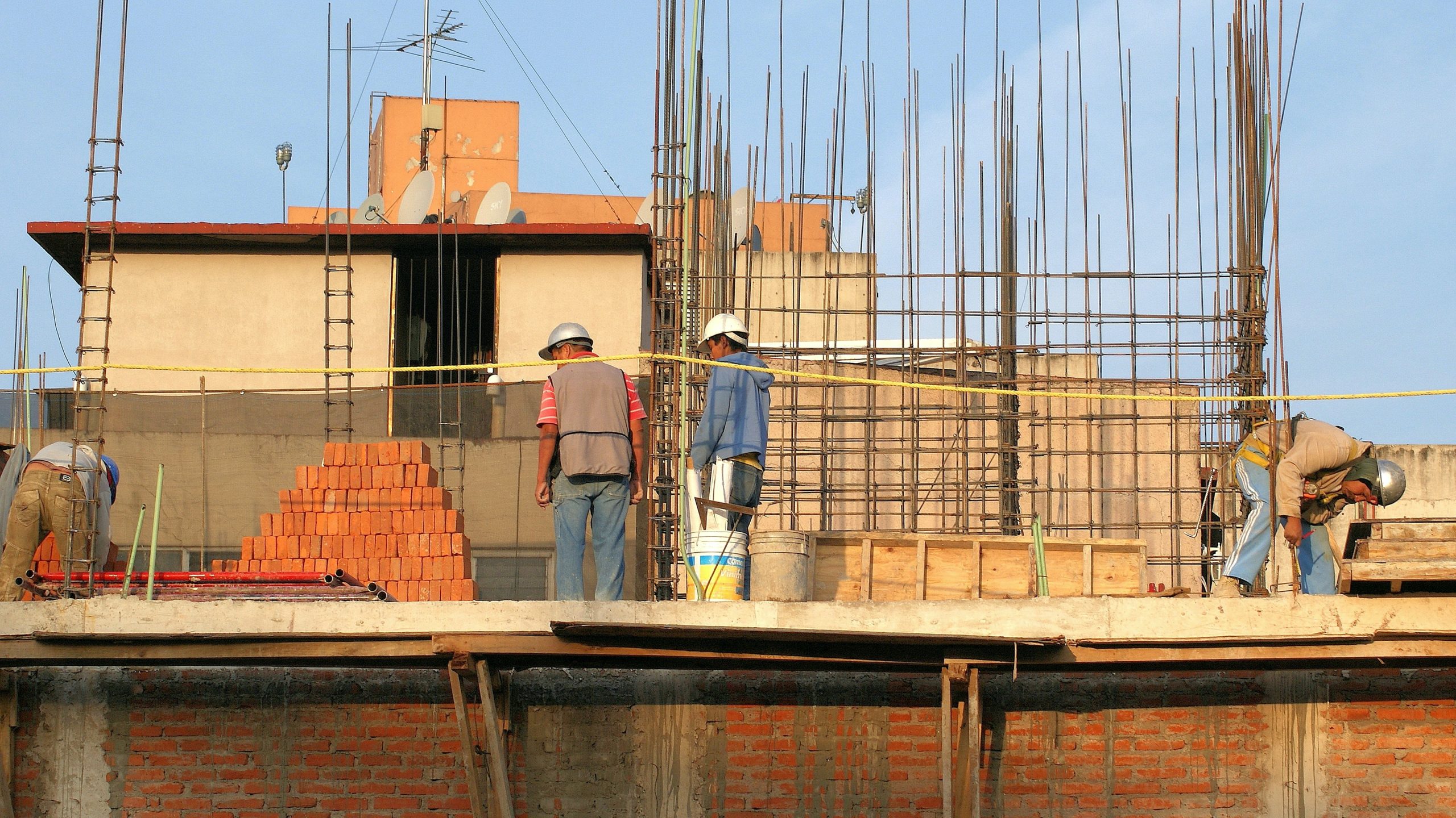 Construction workers standing on second level with scaffolding and bricks.