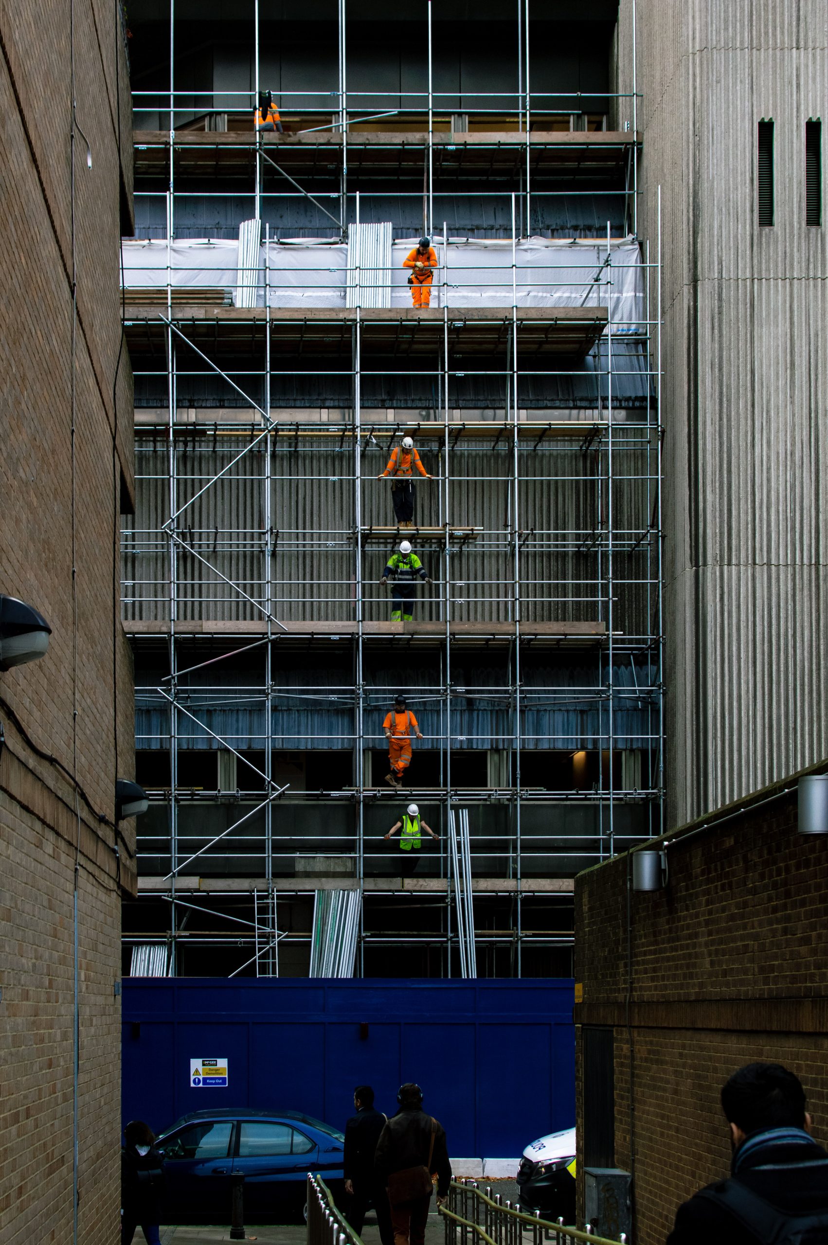 Image of builders lined up on scaffolding on a city building. The workers are outdoors, and vulnerable to extreme heat.