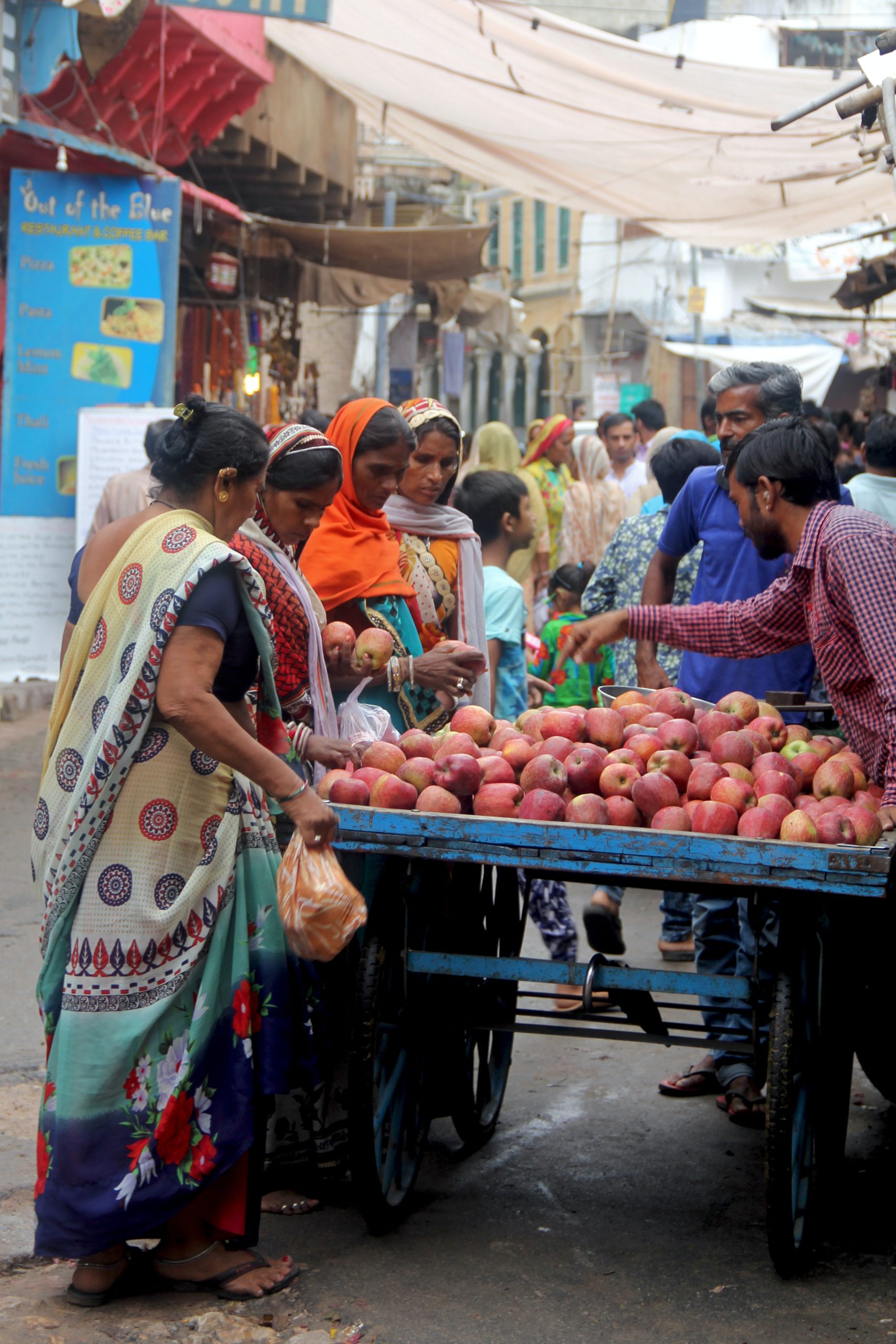 Women shopping at Pushkar main market, looking at a cart of apples.