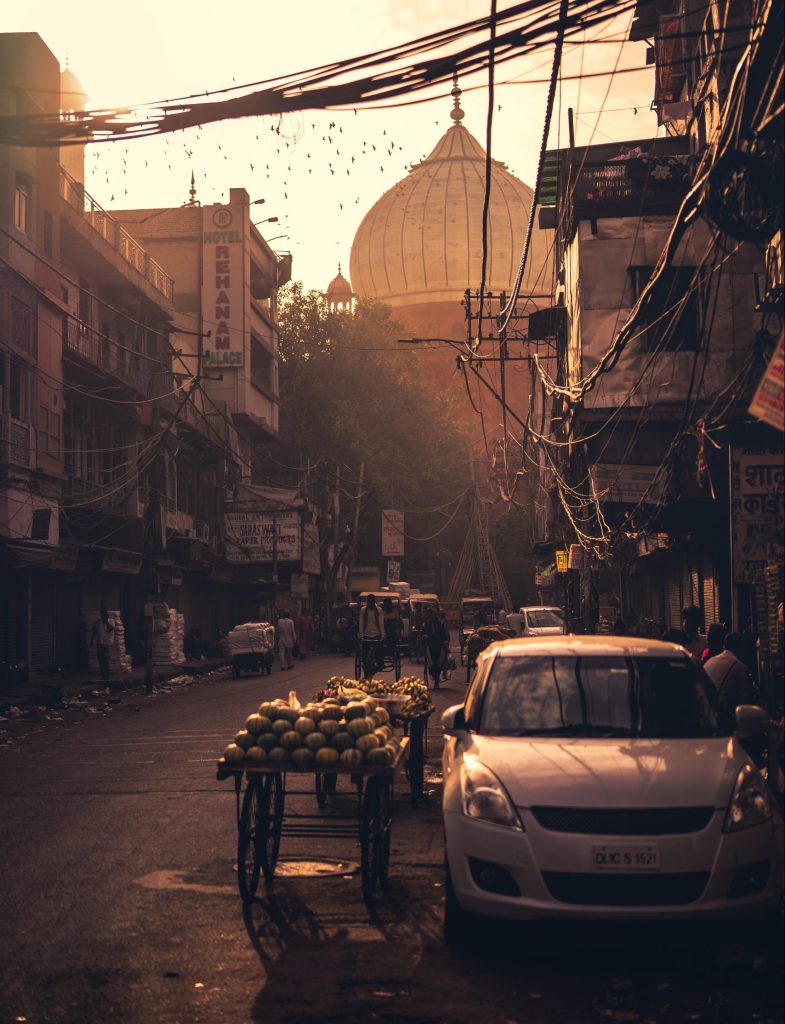 Image of a street in New Delhi. The evening light is yellow. There is a car parked on the right side of the street.