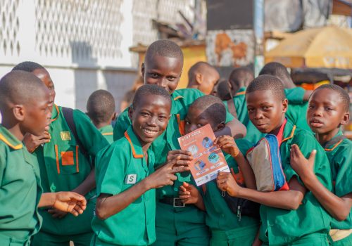 Image of school children in green uniforms holding Freetown's #BeatTheHeat flyers.