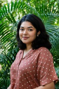 Image of Chief Heat Officer in Dhaka, Bushra Afreen. She wears a brown blouse with polka dots and stands in front of a green, leafy backdrop.