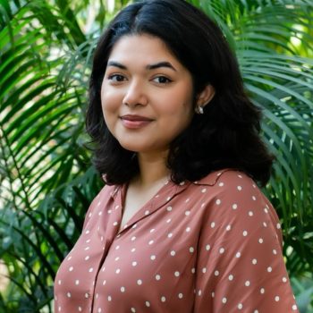 Image of Chief Heat Officer in Dhaka, Bushra Afreen. She wears a brown blouse with polka dots and stands in front of a green, leafy backdrop.