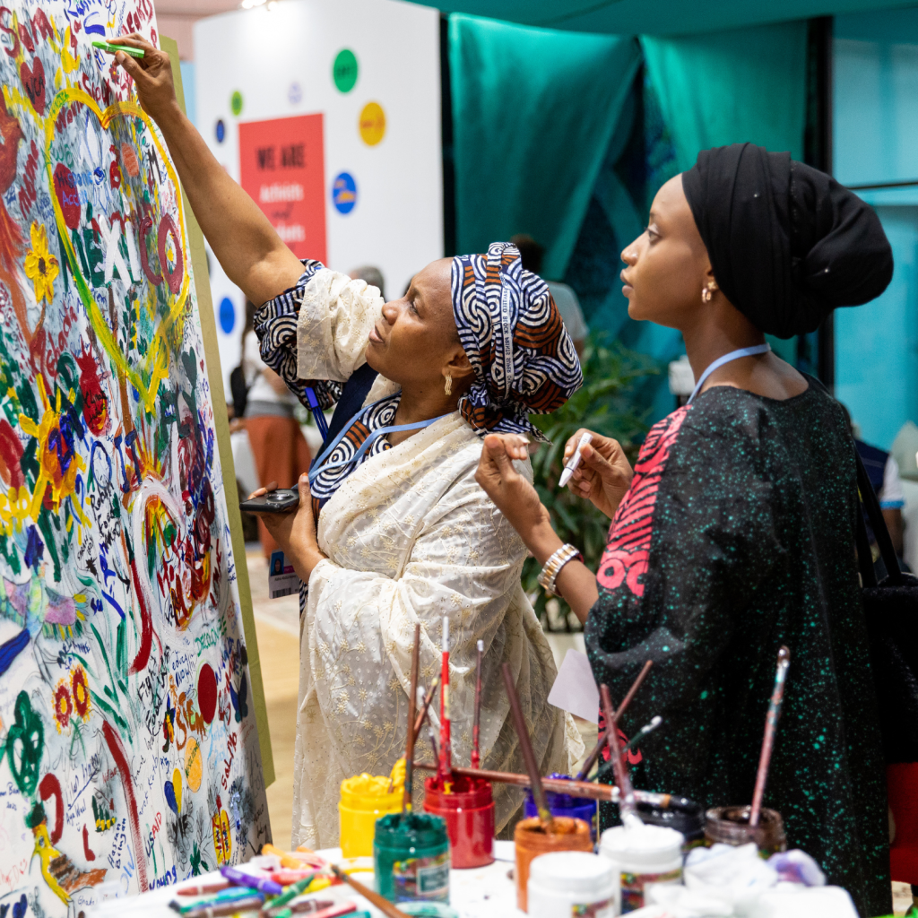 Image of two women adding to the poster of art and drawings.