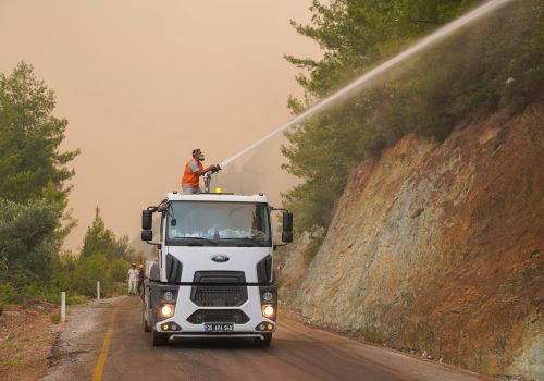 Firefighters in protective gear use a water cannon on a truck to fight a forest wildfire. Photo credit: Özgür Sürmeli on Pexels.